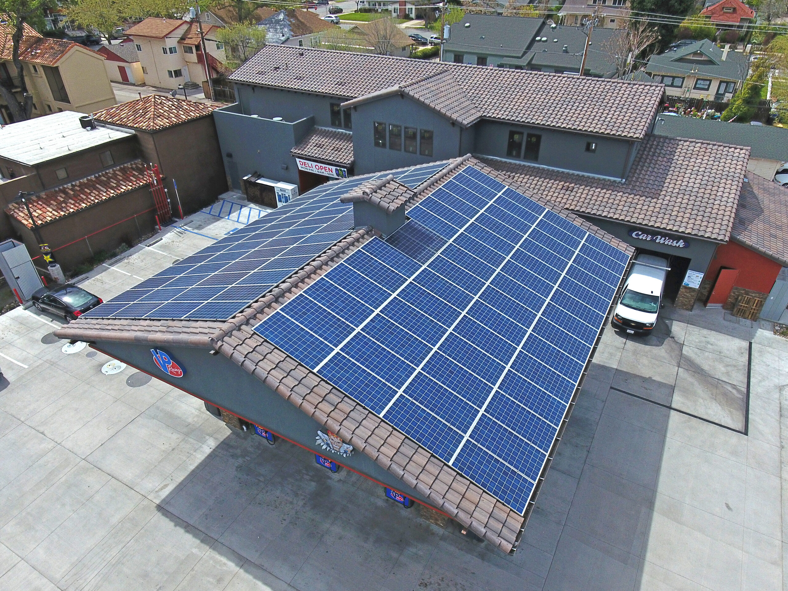 High-angle aerial view of a multi-building residential property with dark blue solar panels completely covering the tiled roof surfaces